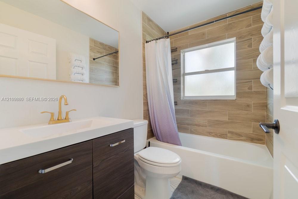 Bathroom featuring a vanity with wood-finish cabinetry, a white integrated countertop, brass-tone faucet, large wall-mounted mirror, and a tub-shower combination with wood-finish tile surround
