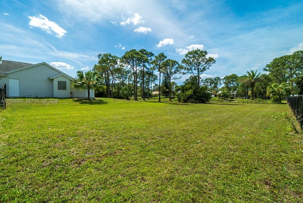 Expansive backyard featuring an open grass lawn, mature trees, and perimeter fencing