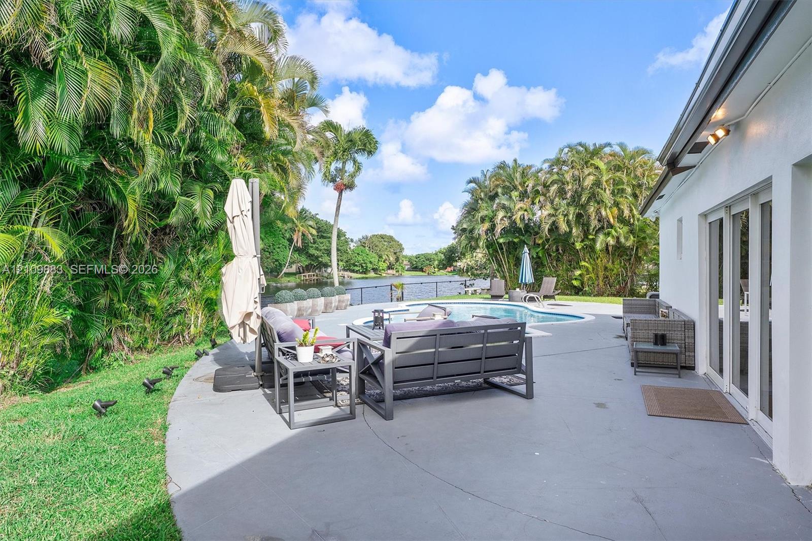 Outdoor living area featuring a paved patio, swimming pool, water frontage, and mature palm landscaping