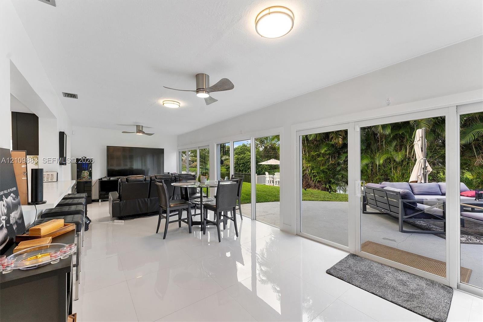 Open-concept living space featuring high-gloss tile flooring, three sets of floor-to-ceiling sliding glass doors, and dual brushed-nickel ceiling fans