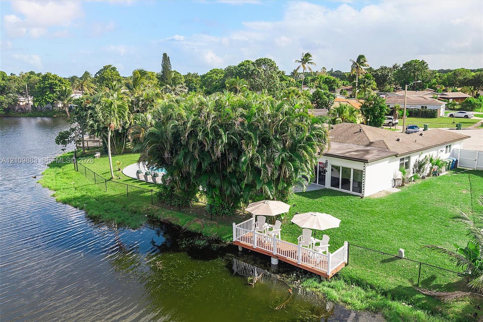Waterfront property featuring a private dock with white railing, a ground-level swimming pool, expansive lawn, mature landscaping, and multi-panel sliding glass doors