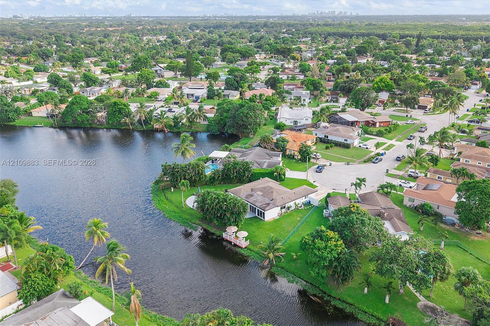Waterfront property featuring a private dock, expansive lawn, mature palm trees, and an in-ground swimming pool