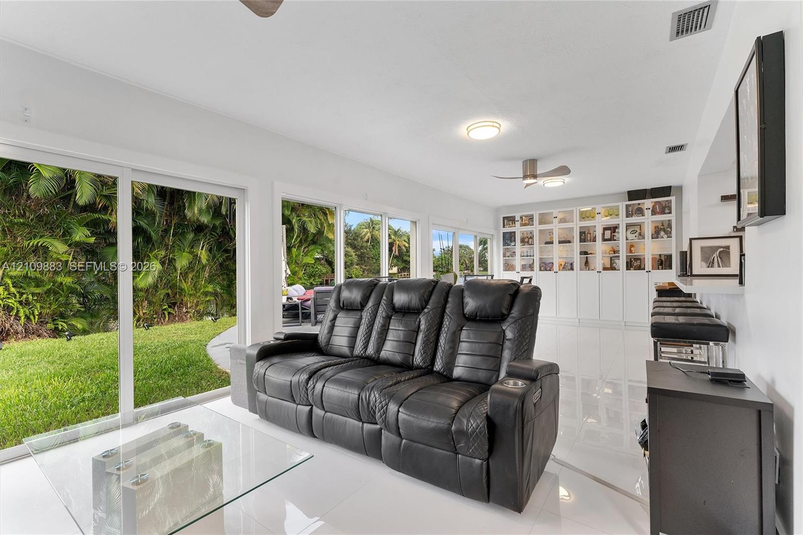 Open-concept living space featuring high-gloss tile flooring, floor-to-ceiling sliding glass doors, built-in white cabinetry, and recessed ceiling lighting