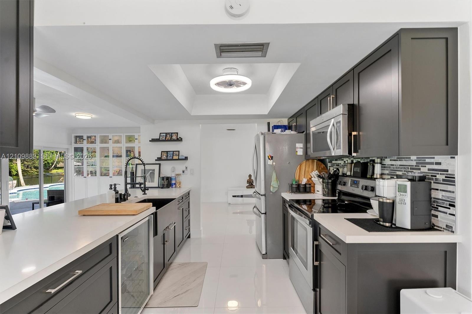 Kitchen featuring charcoal-toned cabinetry, quartz countertops, a farmhouse-style sink with a high-arch faucet, a built-in beverage refrigerator, and a linear mosaic tile backsplash