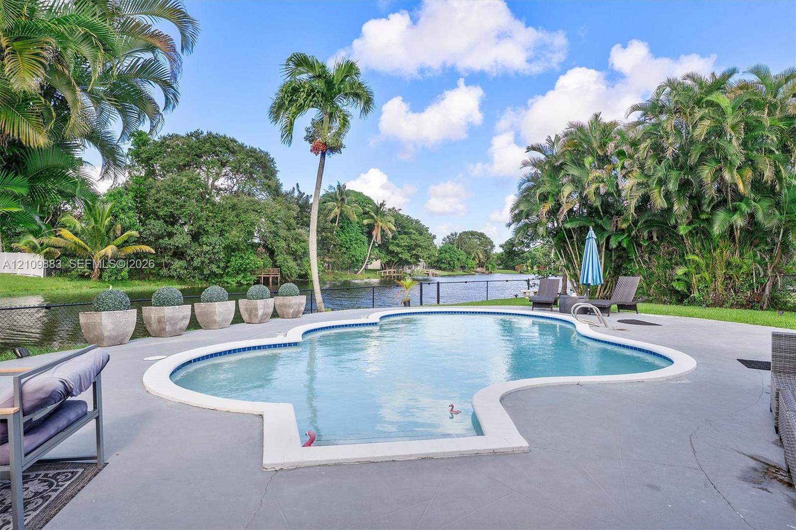 Custom-shaped in-ground pool with concrete surround, bordered by mature landscaping and a canal waterfront setting
