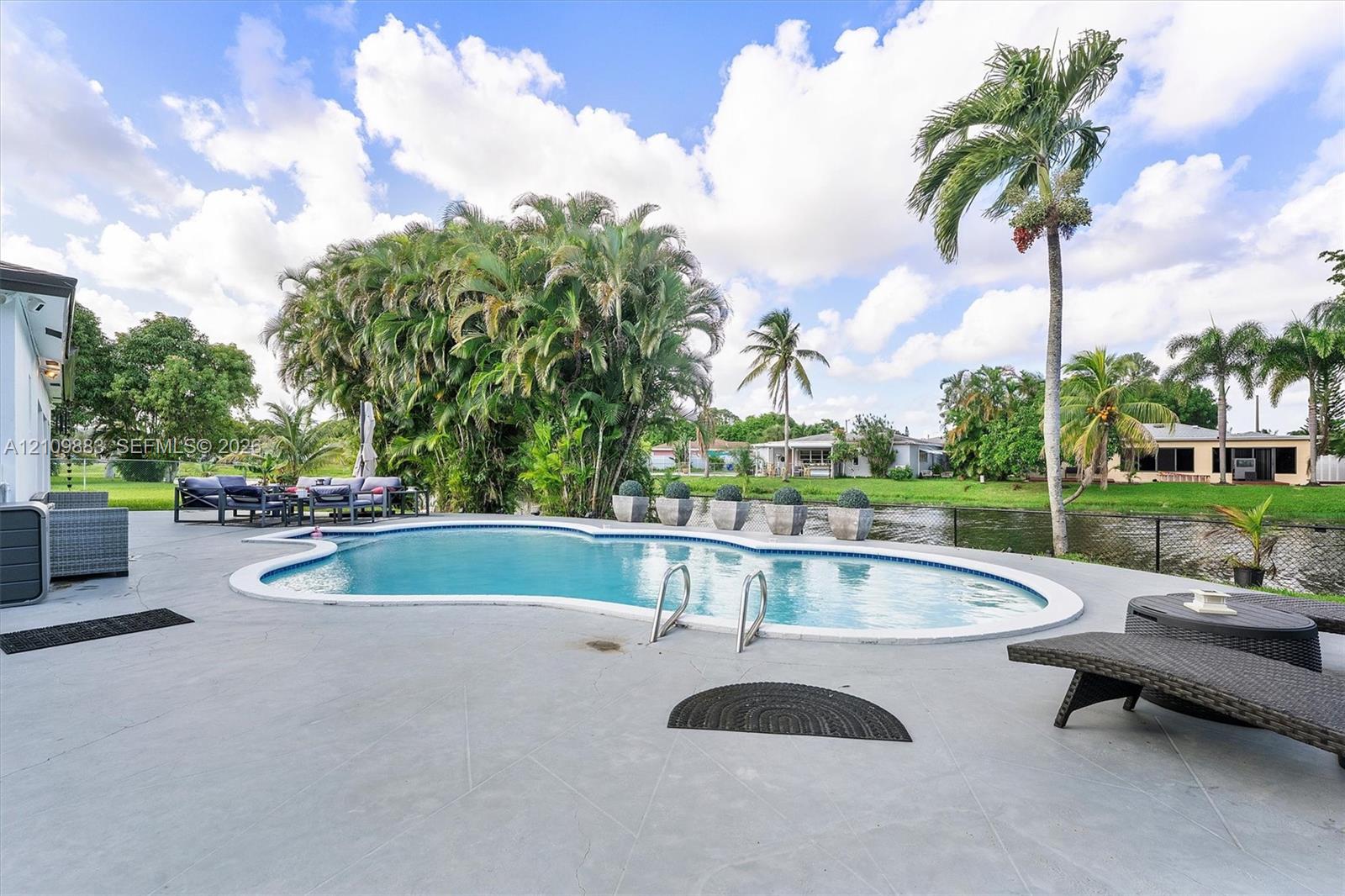 Freeform swimming pool with a concrete pool deck, mature landscaping, and water frontage