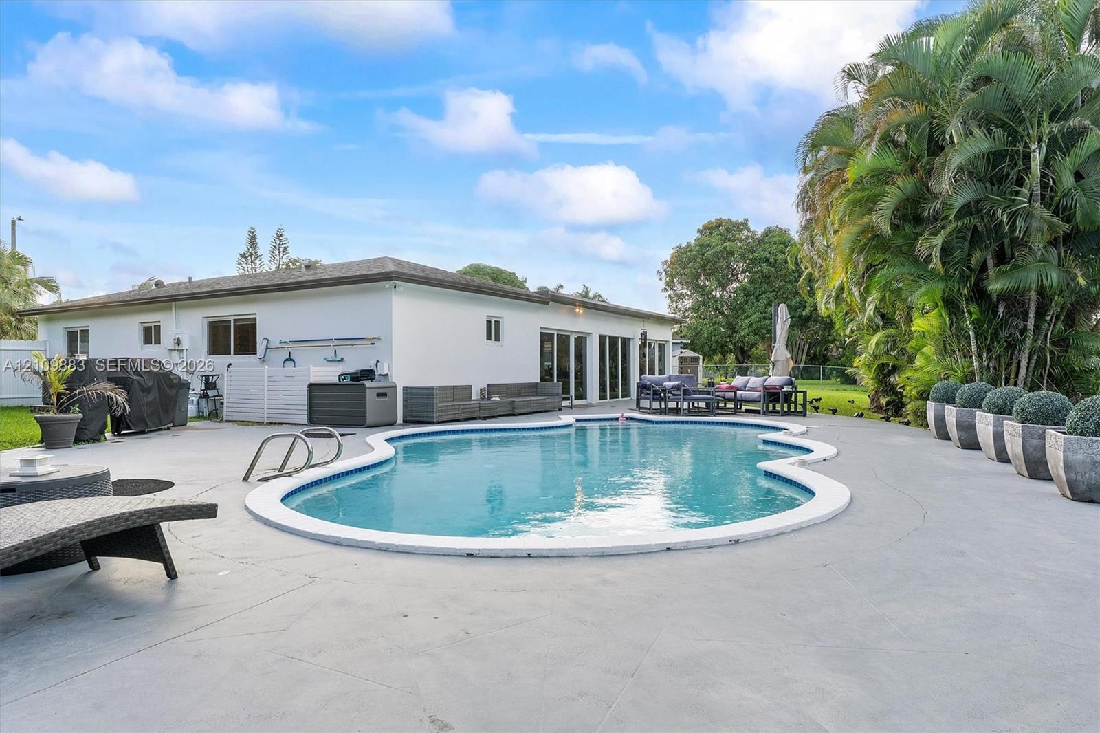 In-ground swimming pool with a curved perimeter, expansive concrete patio, and mature palm trees