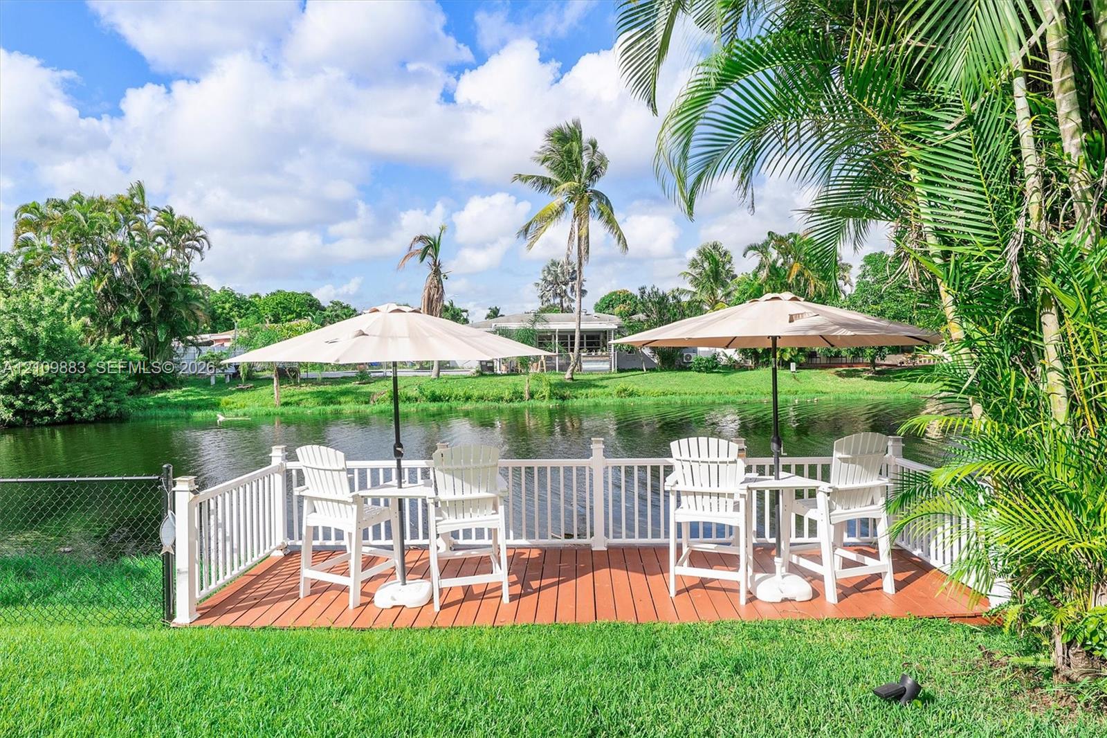 Waterfront deck featuring wood-finish flooring, white picket railing, and manicured landscaping
