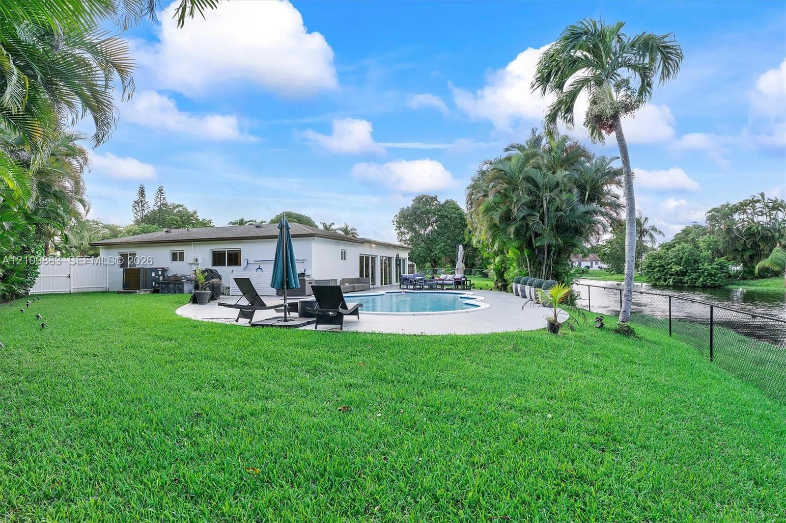 Backyard featuring an in-ground swimming pool, concrete patio, perimeter fencing, and mature palm trees situated along a canal