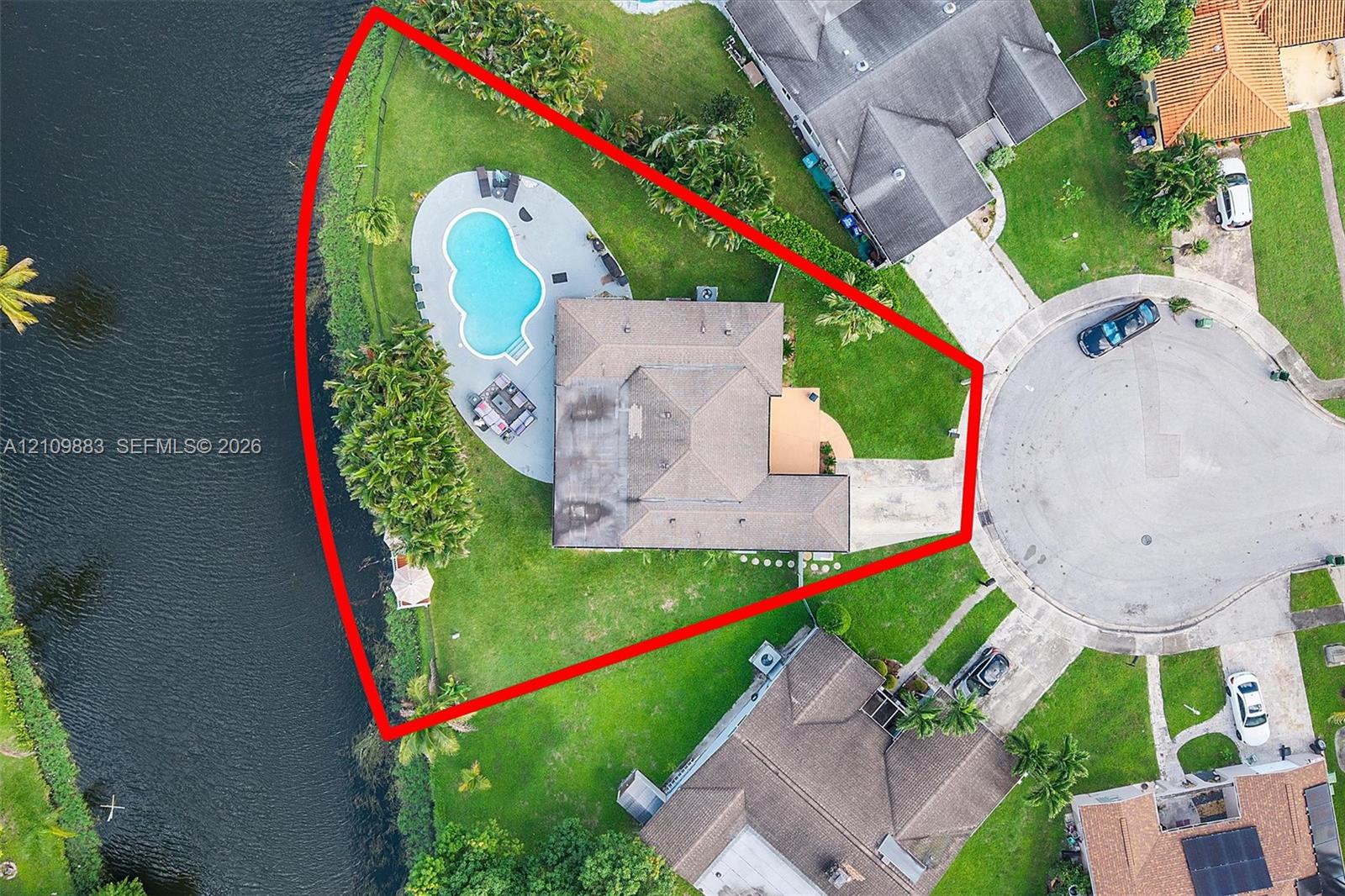 Waterfront lot on a cul-de-sac featuring a paved driveway, expansive lawn, and an in-ground swimming pool with surrounding deck