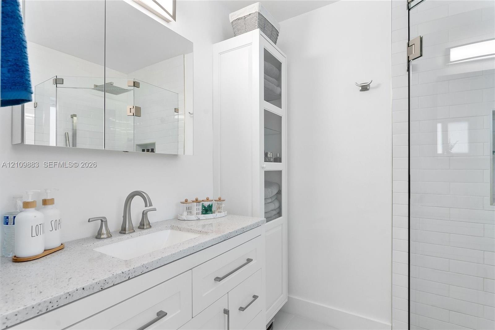 White vanity featuring a solid surface countertop, rectangular undermount sink, brushed nickel widespread faucet, built-in floor-to-ceiling cabinetry, and a frameless glass shower enclosure with white subway tile