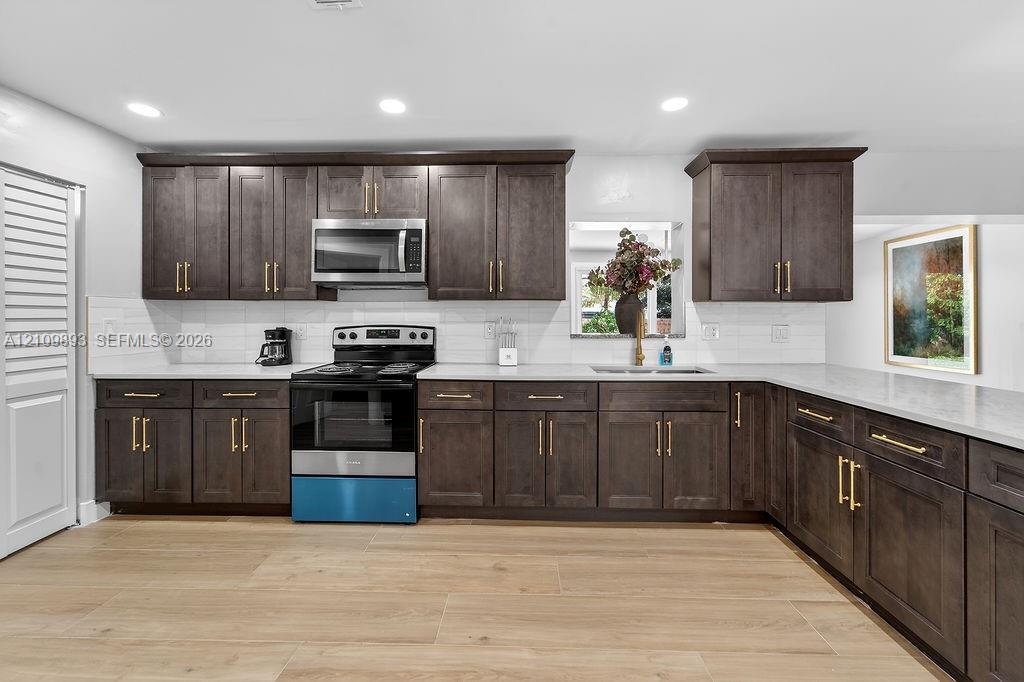 Kitchen featuring dark-finish cabinetry with brass-tone hardware, stone countertops, white subway tile backsplash, stainless steel appliances, and wood-finish flooring