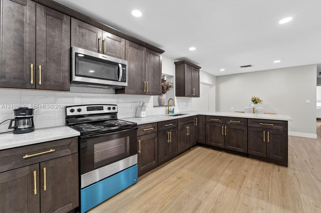Kitchen featuring dark wood-finish cabinetry, quartz countertops, a white tile backsplash, stainless steel appliances, and wood-finish flooring