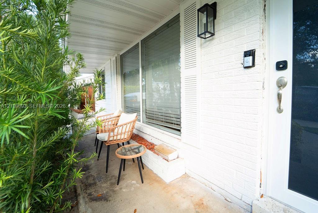 Covered front porch featuring a painted brick exterior, built-in brick planter, decorative shutters, and an exterior wall-mounted lantern