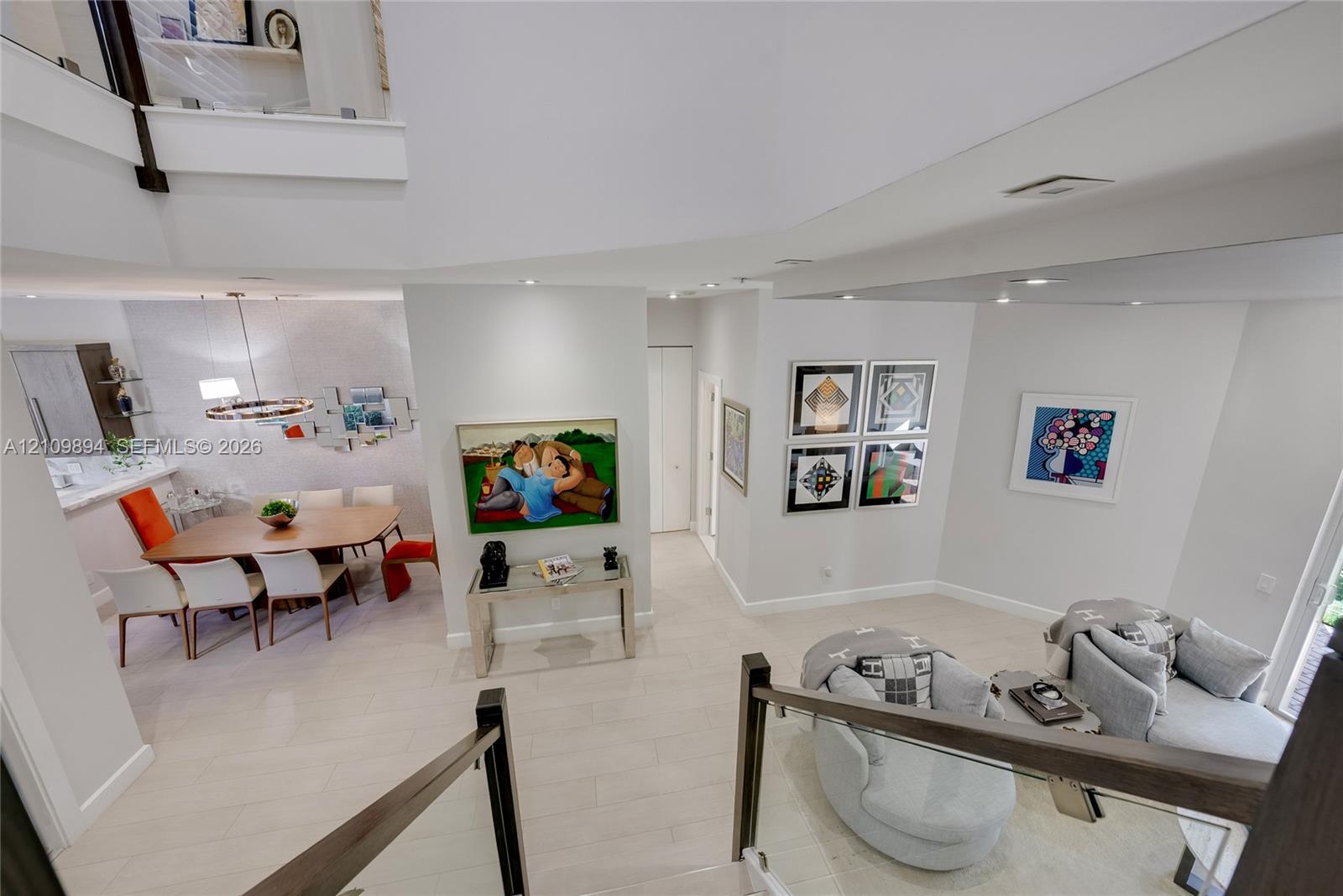 Open-concept living space featuring high ceilings, neutral-toned flooring, glass panel stair railing, and recessed lighting