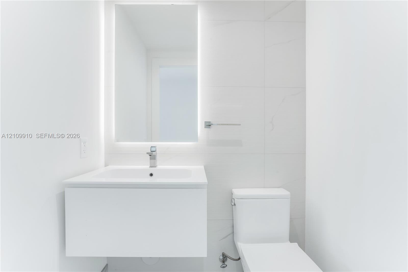 Modern floating vanity with a seamless sink, LED-backlit mirror, and large-format porcelain tile wall cladding