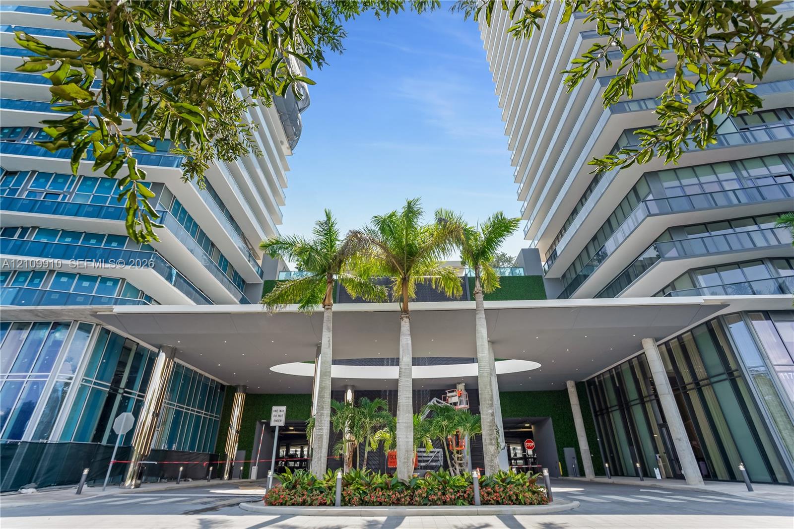 Contemporary high-rise architecture featuring glass facade paneling, covered porte-cochre, recessed lighting, and integrated landscaping with mature palm trees