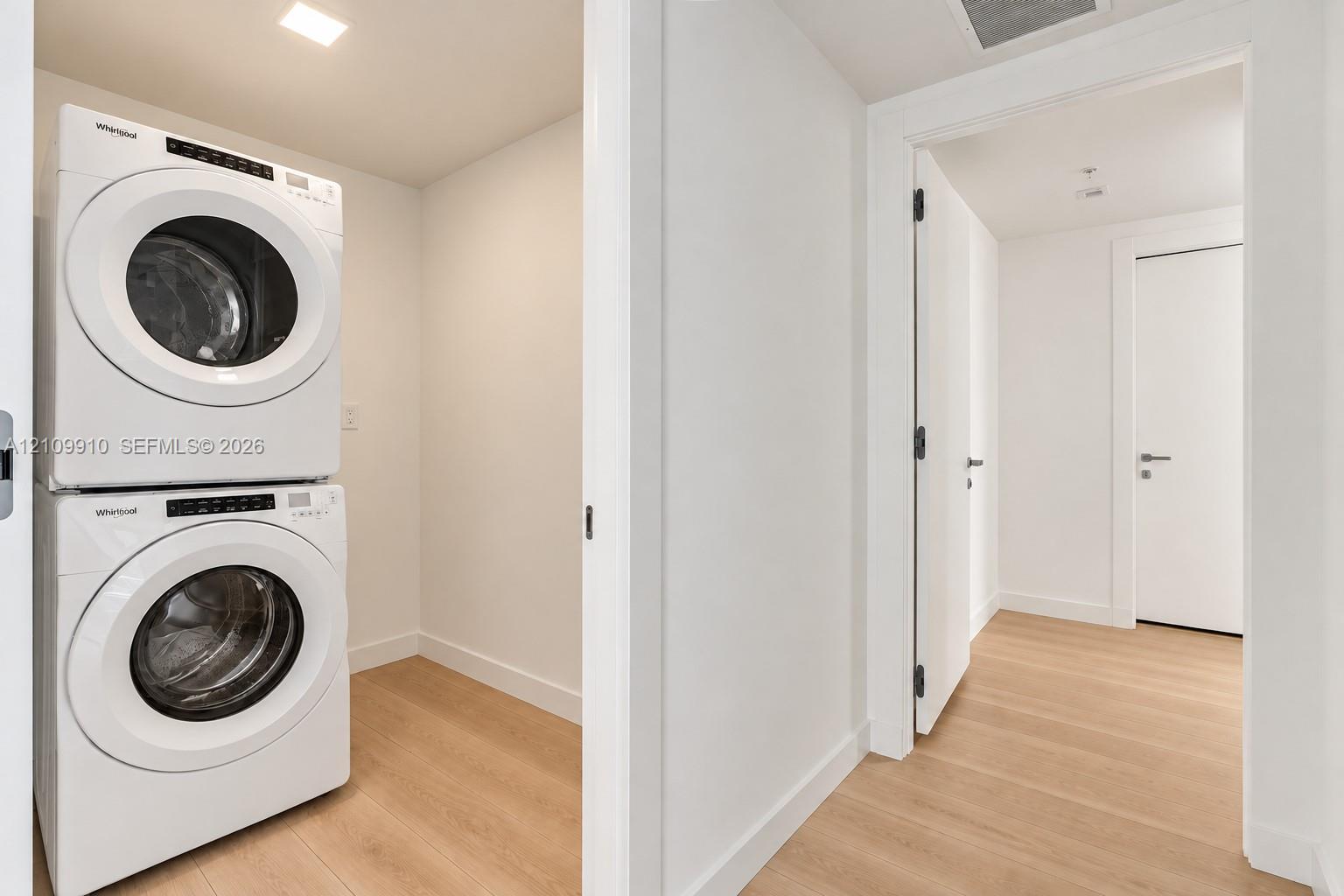 Utility space featuring a stacked white laundry unit, recessed ceiling lighting, and wood-finish flooring