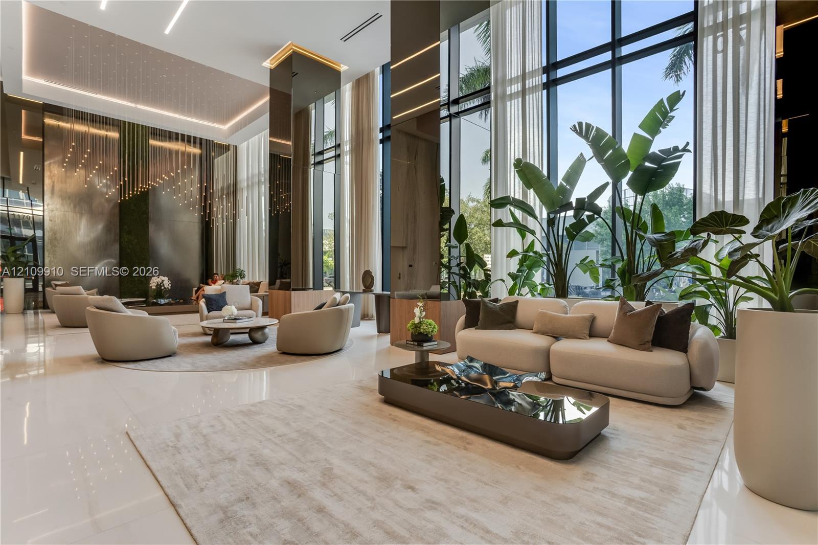 Double-height floor-to-ceiling windows, polished stone flooring, recessed ceiling lighting, reflective wall paneling, and architectural metallic accent features