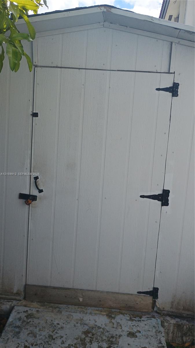 Vertical white exterior siding, gable roofline, and black metal door hardware including hinges and a handle