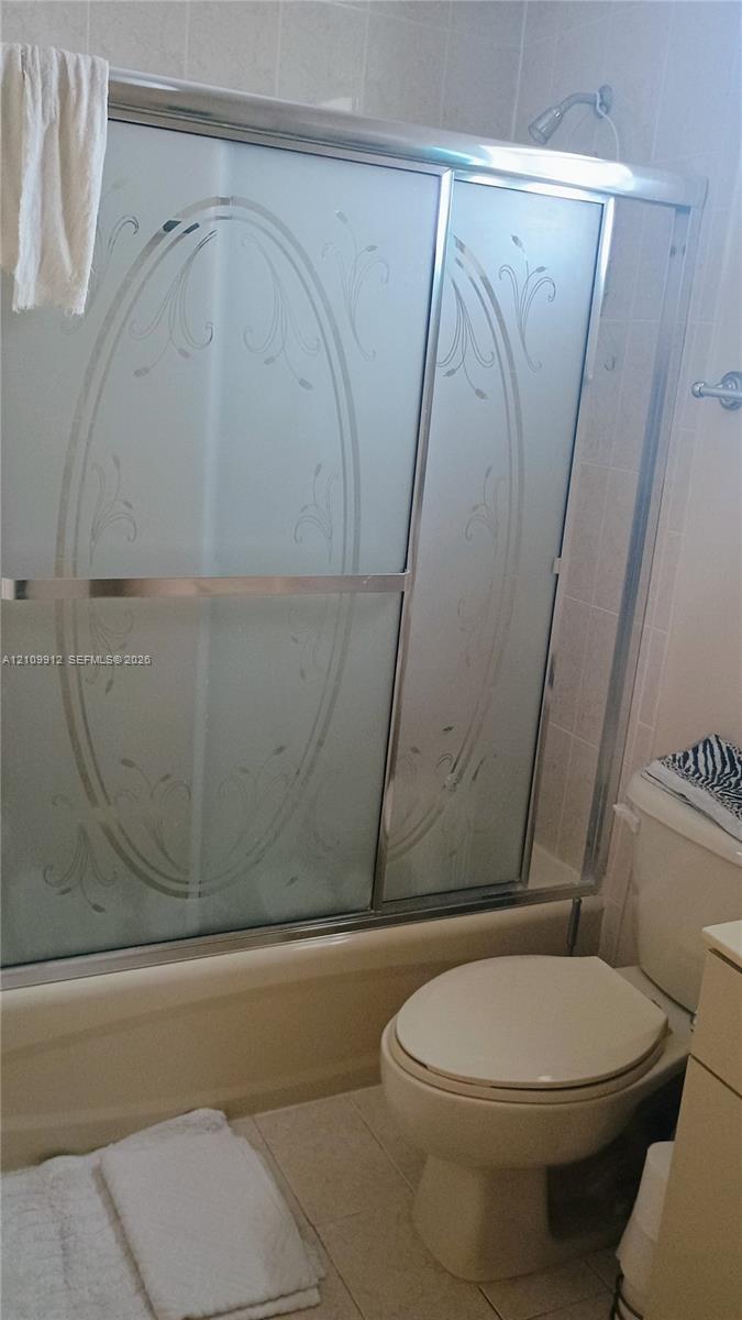 Bathtub and shower combination featuring sliding frosted glass doors with etched detailing, chrome-finished hardware, and tile wall surround