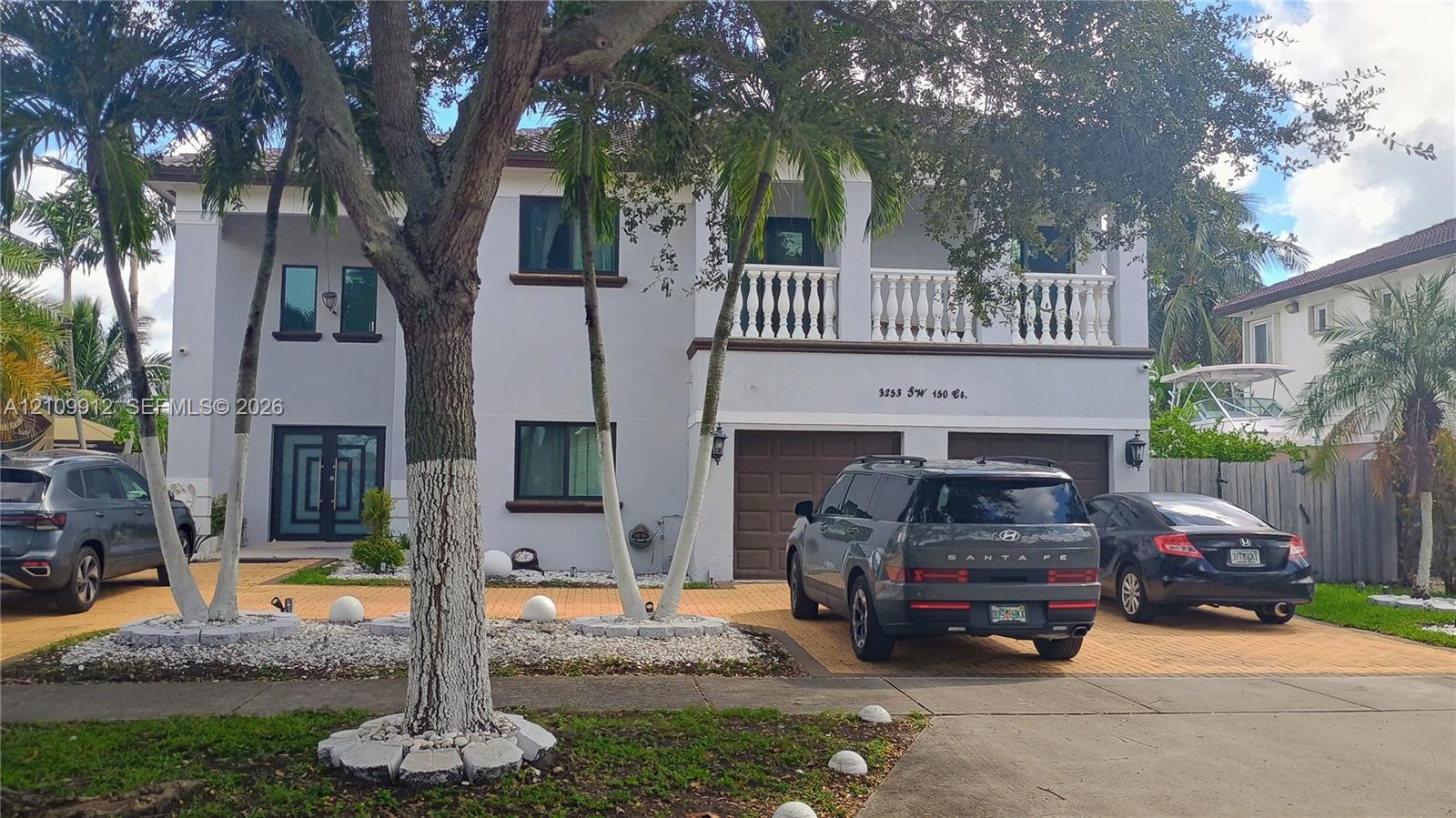 Two-story residence featuring a paved driveway, a double-car garage, an upper-level balcony with white balustrades, and double-door entryway