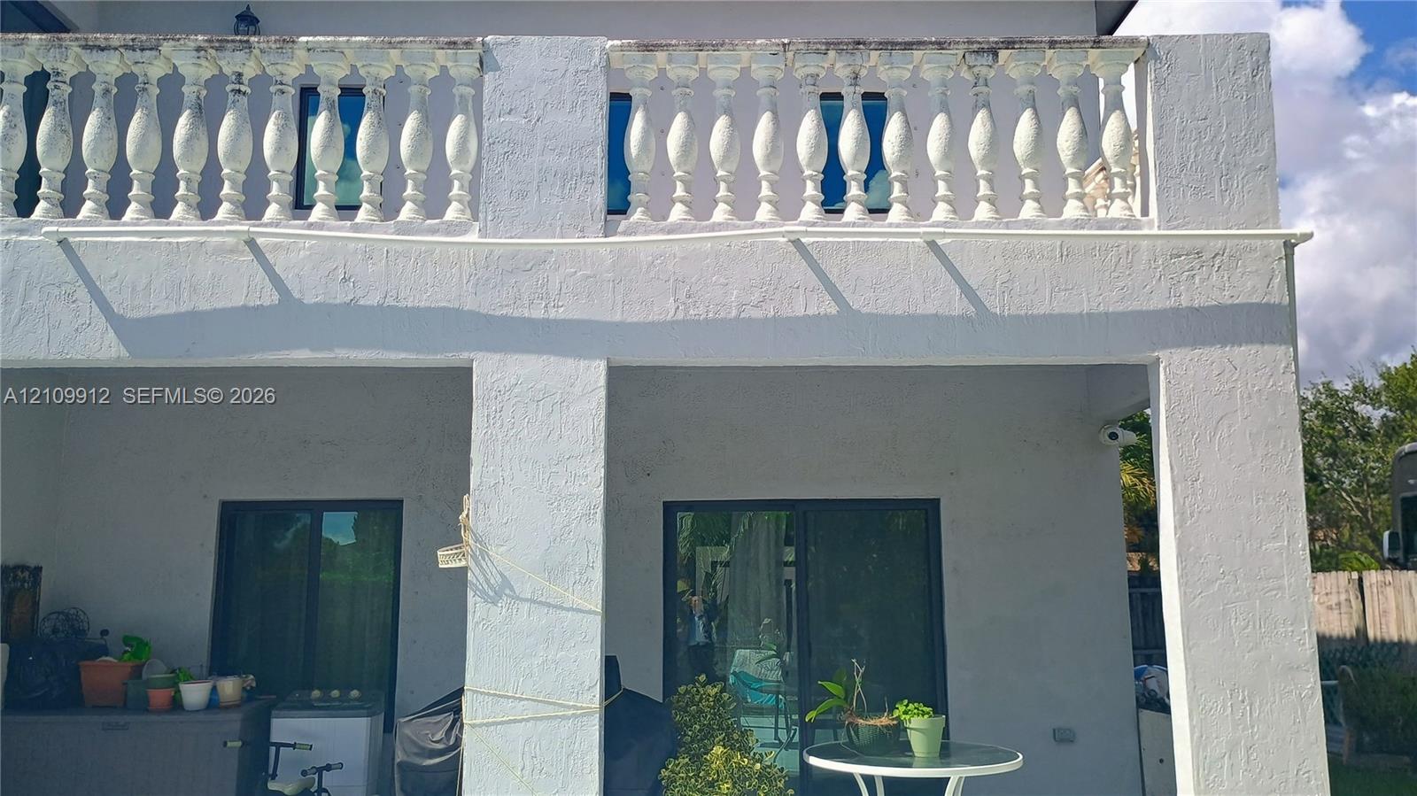 Stucco exterior featuring a covered patio, a second-story balcony with decorative balustrade, and dual glass sliding doors