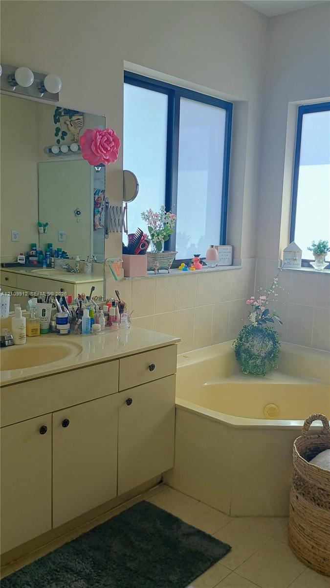 Bathroom featuring a corner soaking tub, solid-surface vanity countertop with integrated sink, wooden cabinetry, and dual windows