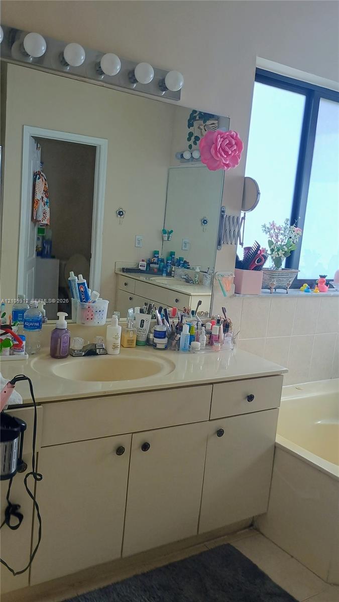 Bathroom vanity featuring a solid-surface countertop with an integrated basin, multi-door cabinetry with dark hardware, a large wall-to-wall mirror, and a five-bulb vanity light fixture