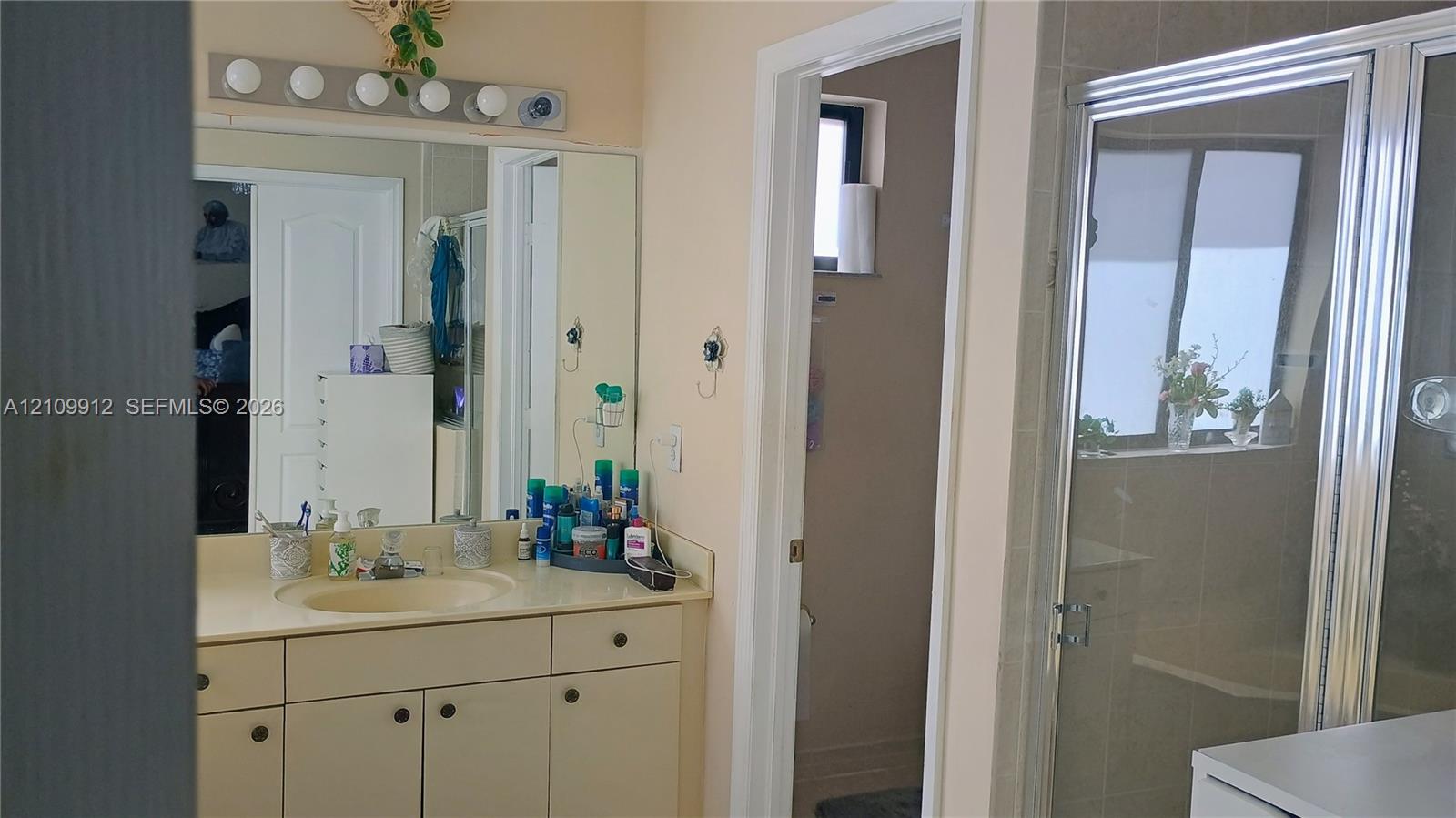 Bathroom featuring a vanity with integrated sink, large wall-mounted mirror, multi-bulb light fixture, and a glass-enclosed shower