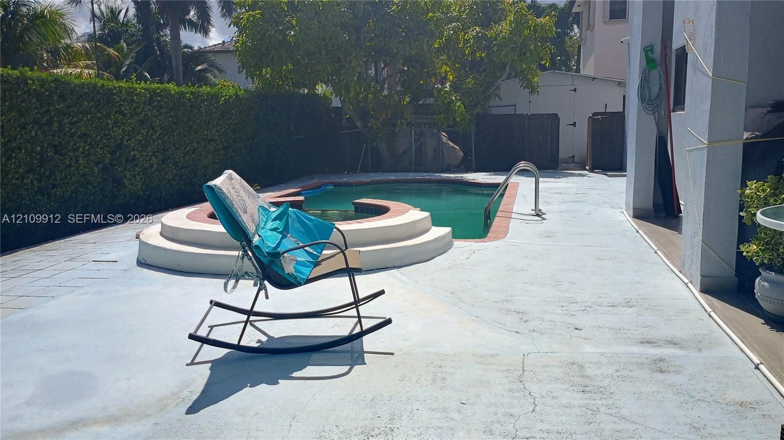 Outdoor area featuring an in-ground swimming pool with an integrated spa, concrete patio, and mature perimeter hedging