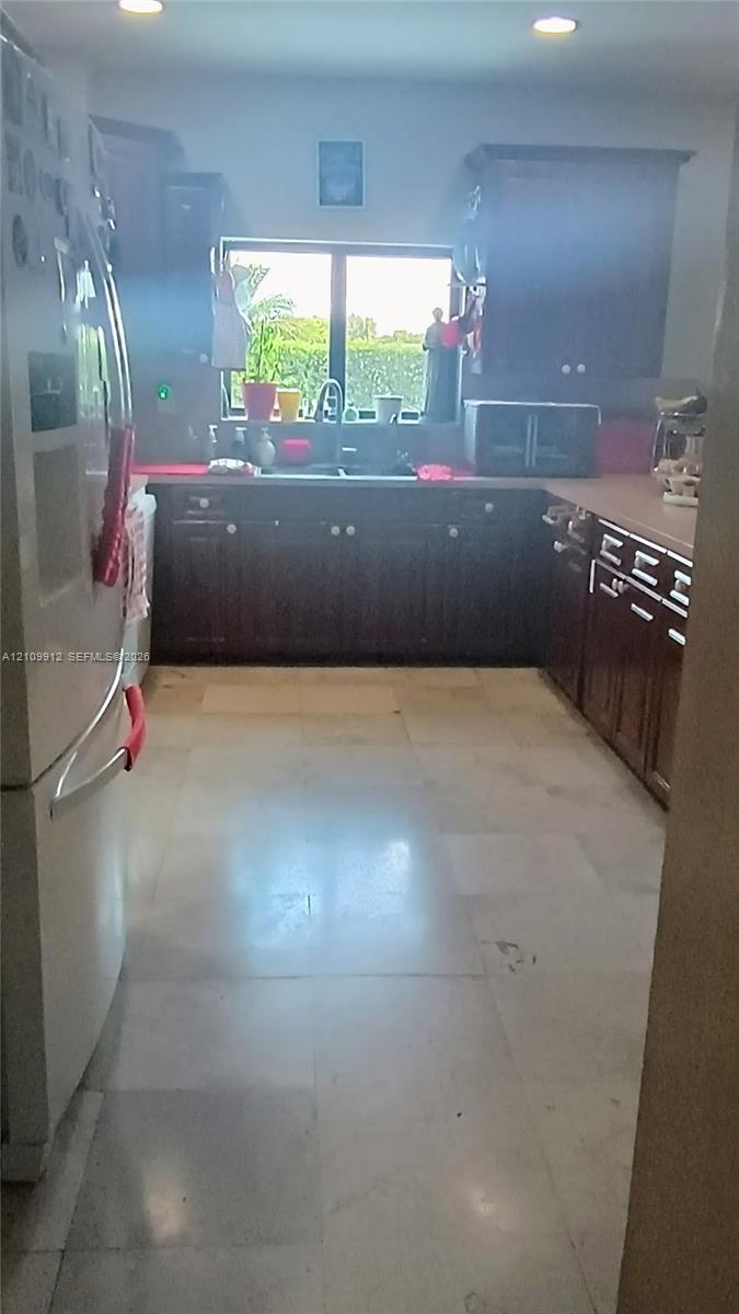 Kitchen featuring dark-finish cabinetry, neutral tile flooring, recessed ceiling lighting, and a double-basin sink positioned beneath a window