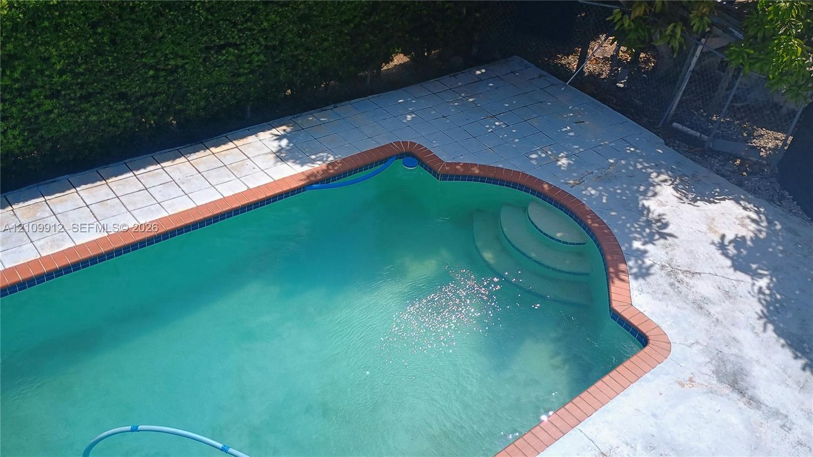 In-ground pool featuring a brick coping border and concrete surround with integrated entry steps