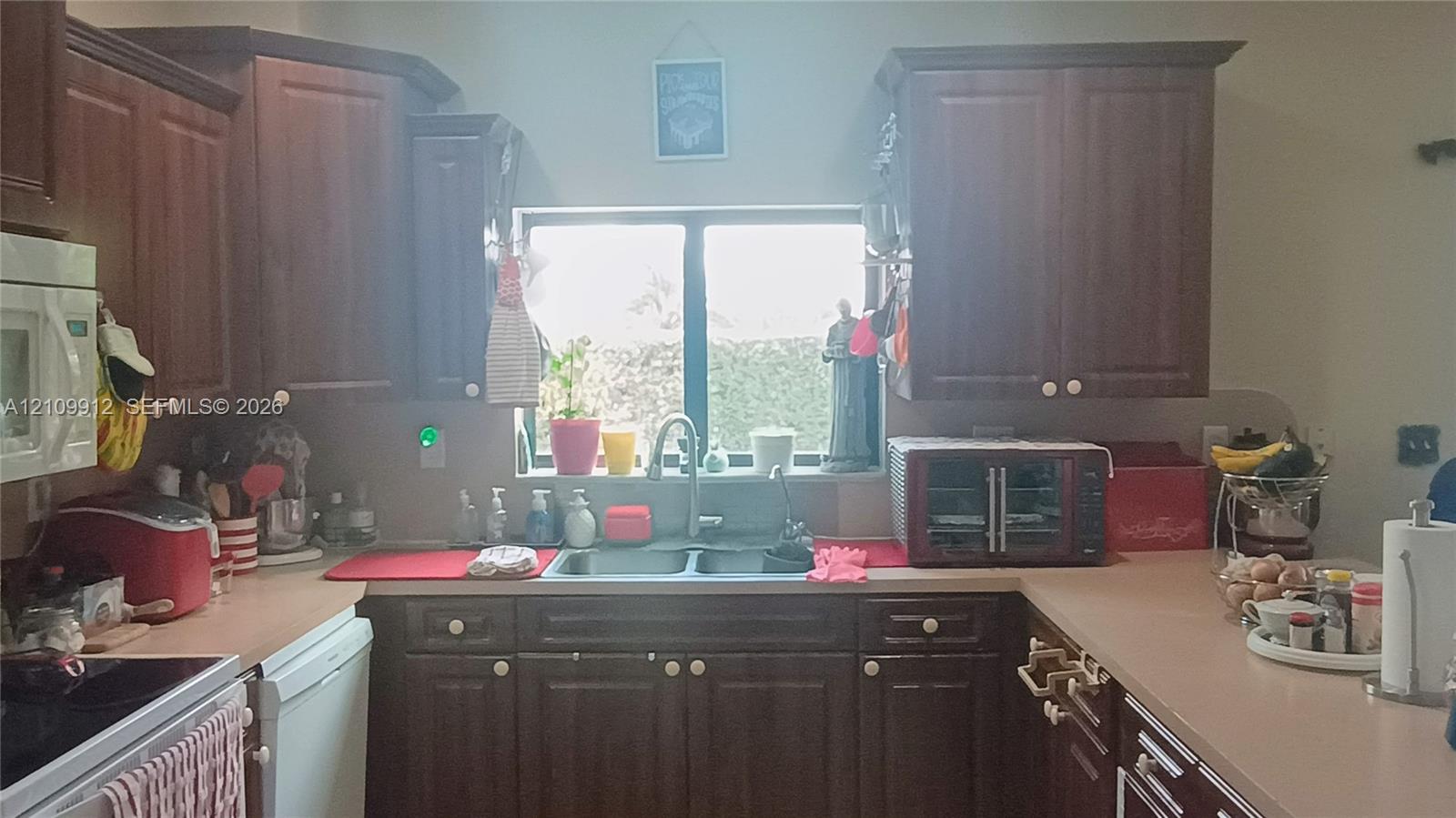 Kitchen featuring dark wood-finish cabinetry, solid-surface countertops, dual-basin stainless steel sink with pull-down faucet, and built-in microwave