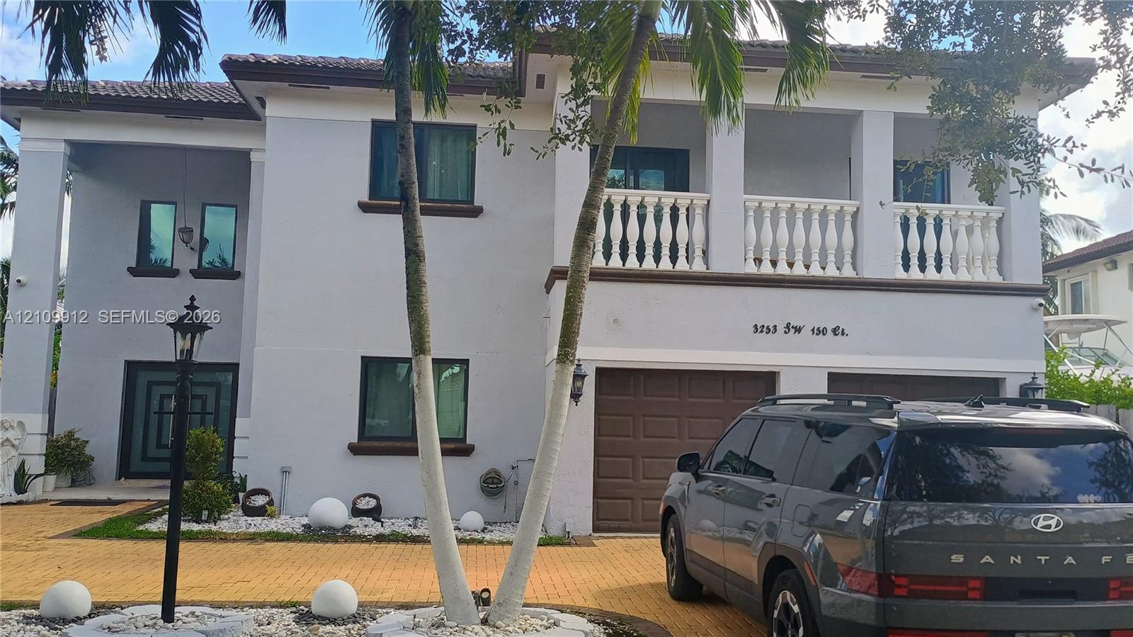 Two-story residence featuring a paved driveway, a second-floor balcony with balustrade railing, a tiled roof, and a two-car garage