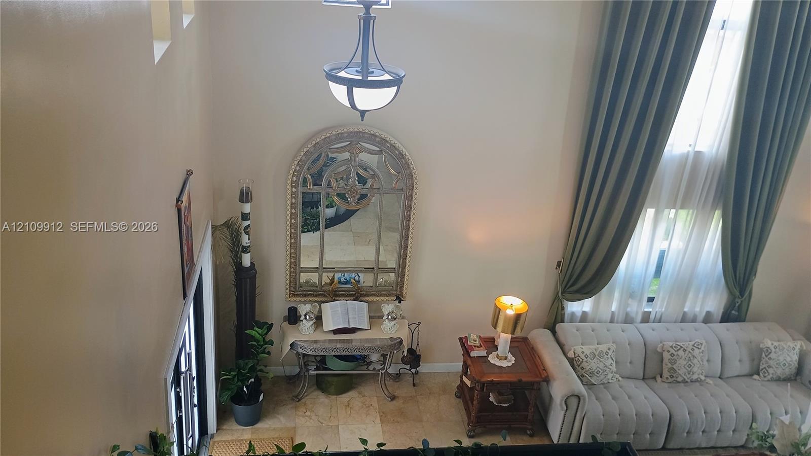 Double-height ceiling, floor-to-ceiling drapery, stone-finish tile flooring, and decorative wrought-iron chandelier