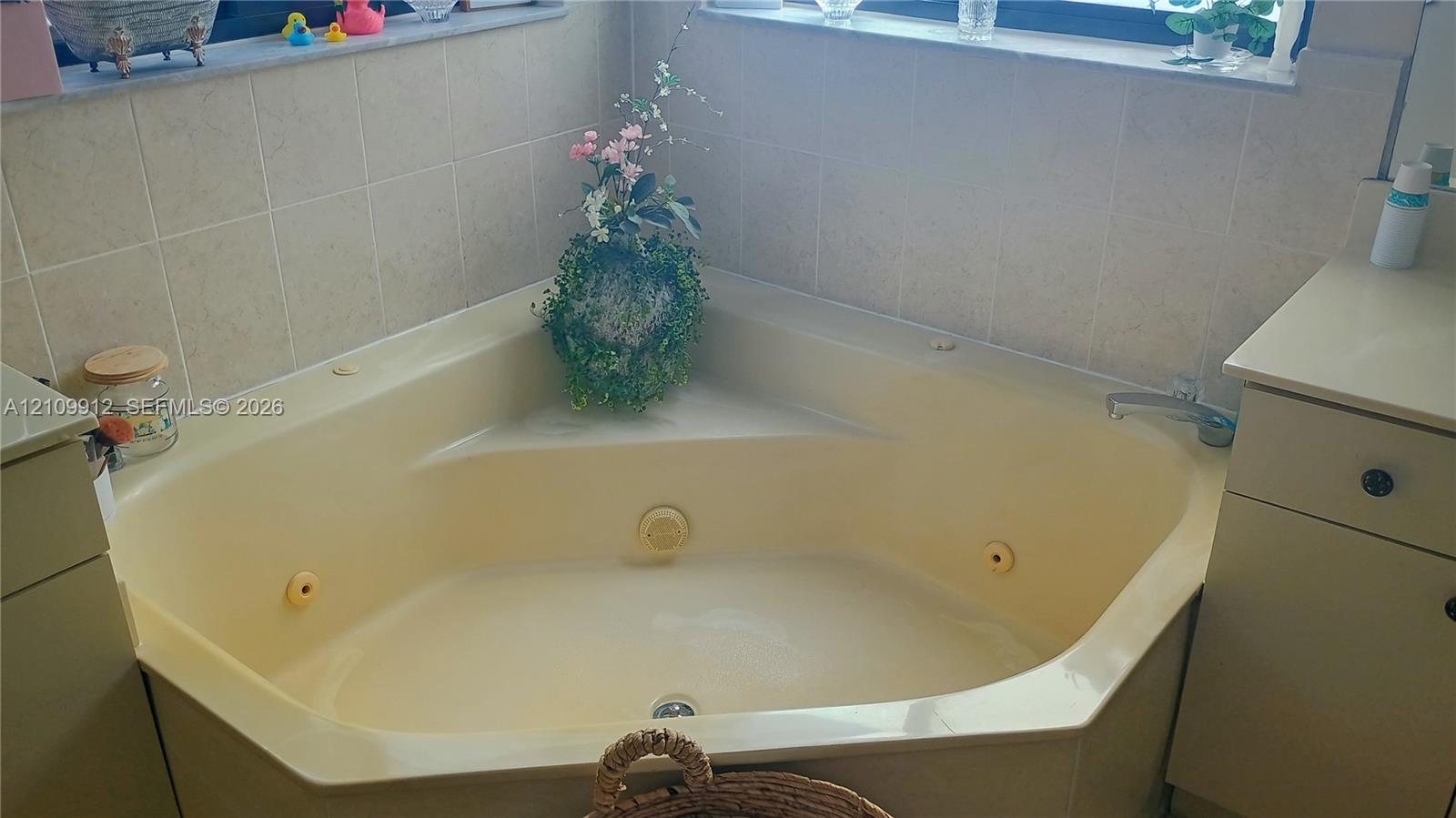 Corner soaking tub with integrated jet features, surround tile backsplash, and solid-surface vanity cabinetry
