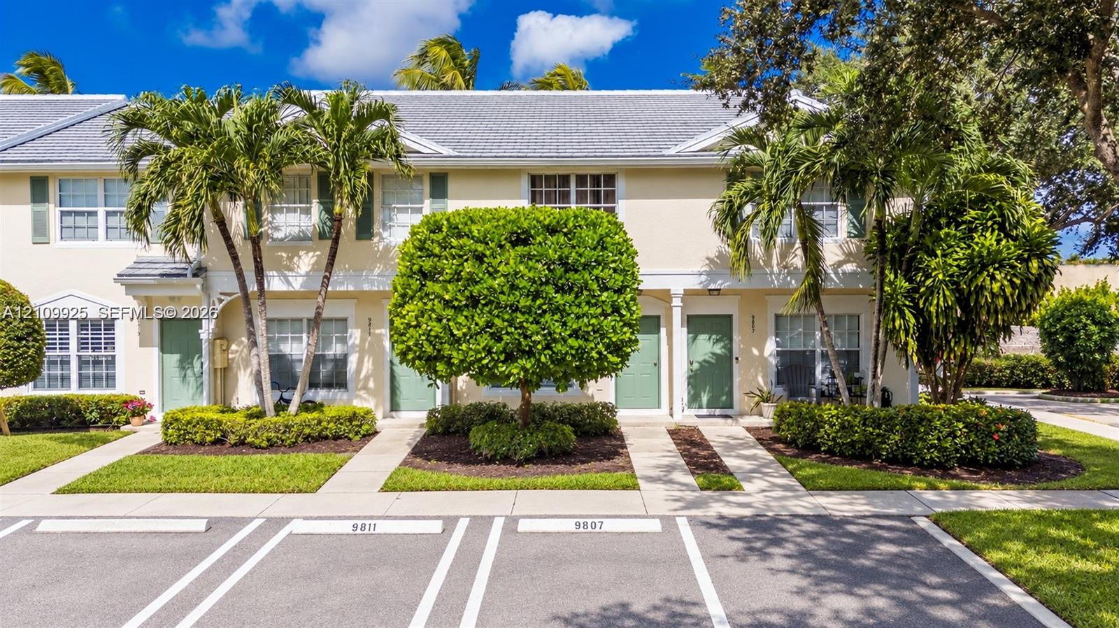Two-story townhome exterior featuring light-toned stucco siding, a grey shingle roof, multi-pane windows, and designated asphalt parking Two-story townhome exterior featuring light-toned stucco siding, a grey shingle roof, multi-pane windows, and designated asphalt parking