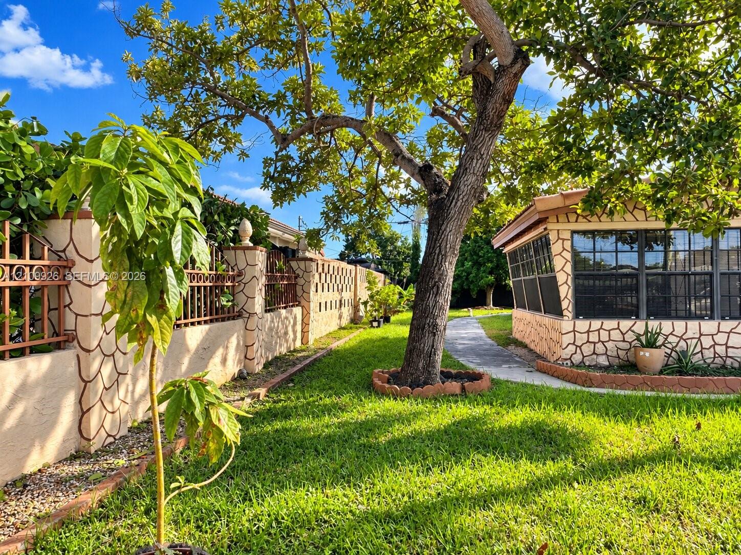 Exterior area featuring stone-clad masonry walls, a screened-in structure with grid windows, mature landscaping, and a concrete pathway