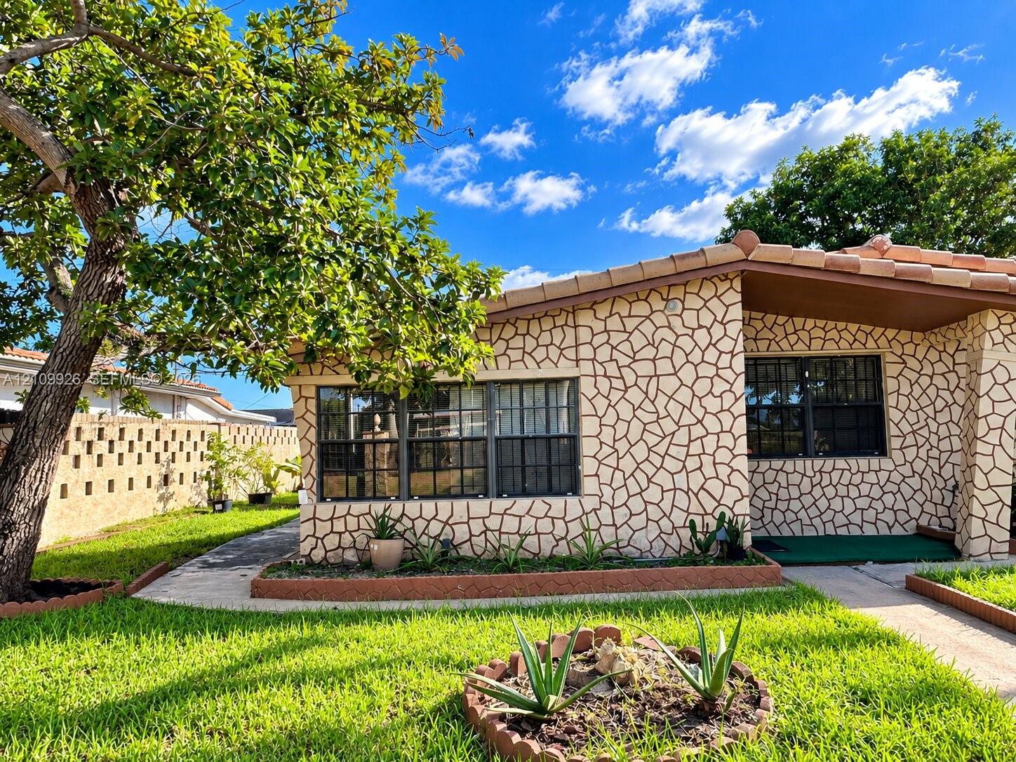 Exterior featuring decorative stone-patterned facade, mission-style tile roof, multi-pane windows, and a landscaped front yard with concrete border edging