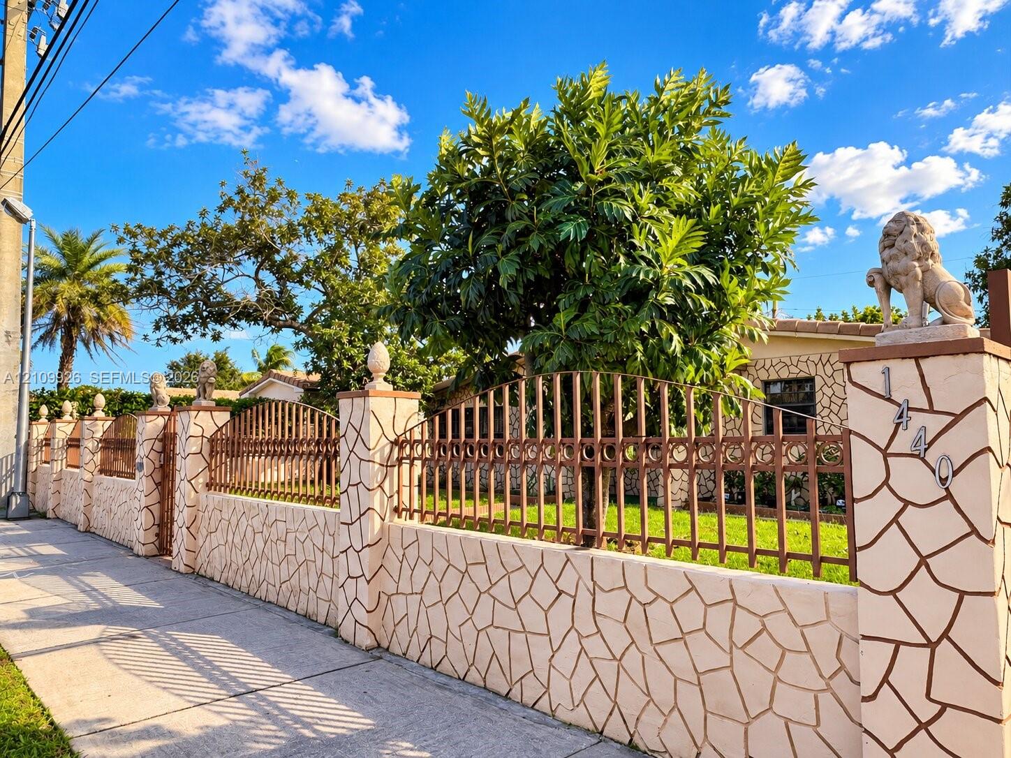 Custom masonry boundary wall featuring decorative stone cladding, ornamental metal fencing, and integrated stone lion statuary