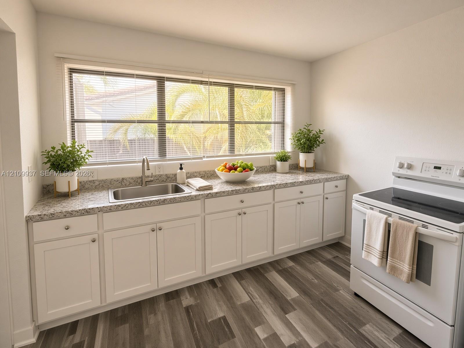 Kitchen featuring white shaker-style cabinetry, stone-finish countertops, stainless steel undermount sink, wood-finish flooring, and a wide window with natural light