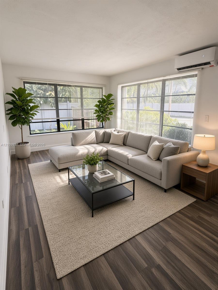 Living area featuring wood-finish flooring, large multi-pane windows, and a wall-mounted ductless climate control unit