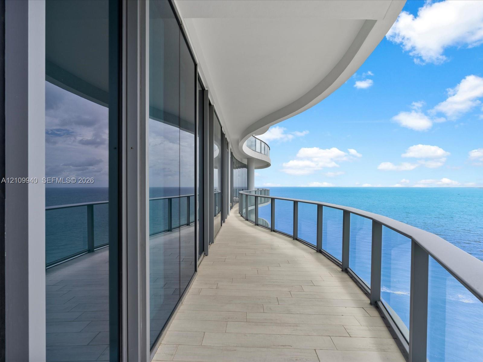 Curved exterior terrace featuring floor-to-ceiling glass panel walls, light-toned tile flooring, and metal-framed glass railings
