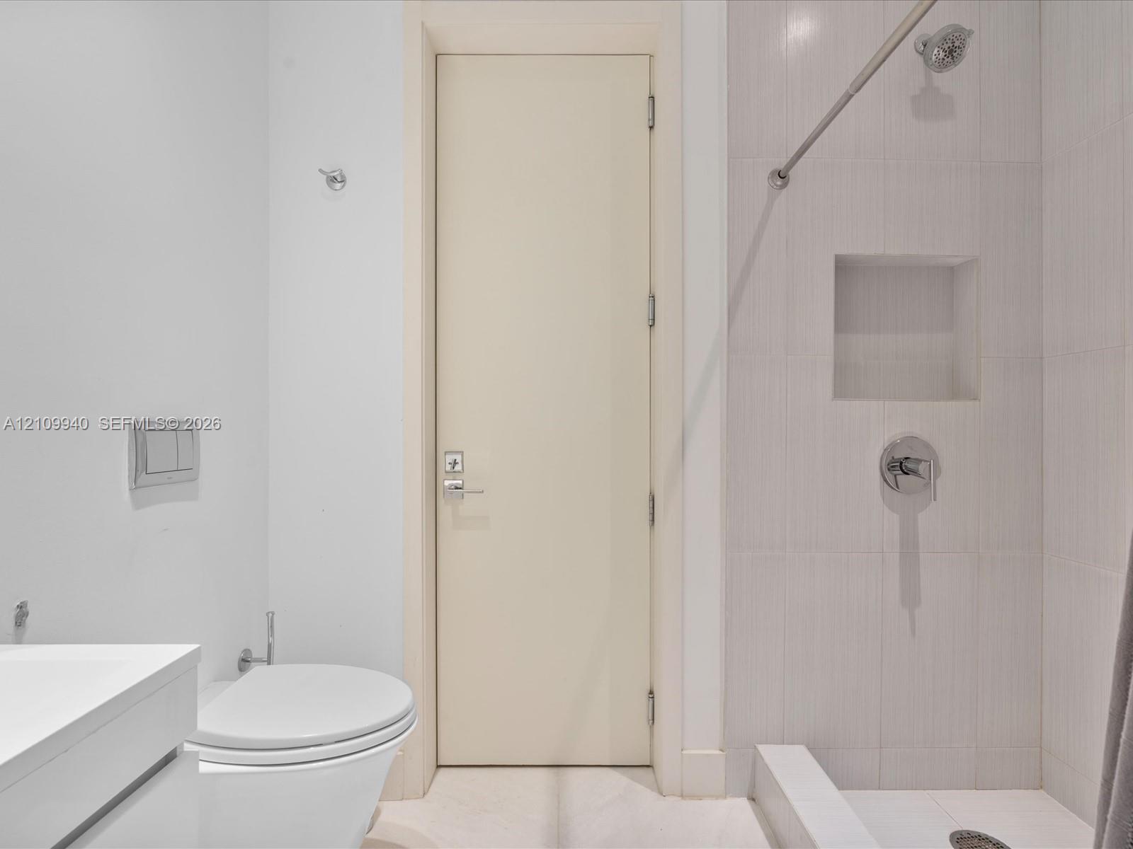 Bathroom featuring a wall-mounted dual-flush toilet, a floating vanity with a white basin, and a tiled shower with a built-in recessed niche and chrome fixtures