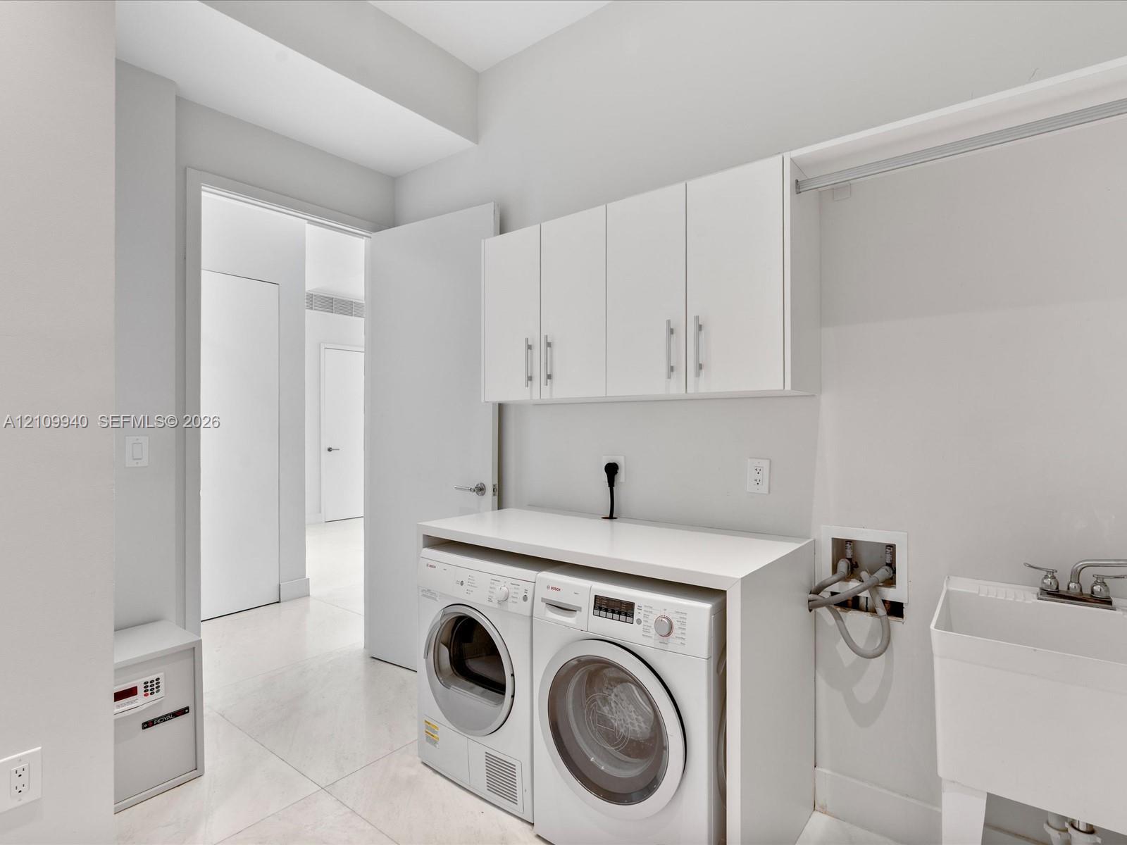 Laundry area featuring white cabinetry with silver-tone hardware, a solid-surface countertop, an integrated clothing rod, and a utility sink with a dual-handle faucet