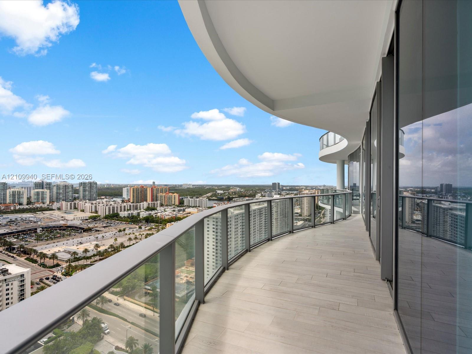 Curved balcony featuring light-toned tile flooring, floor-to-ceiling glass doors, and a sleek metal railing
