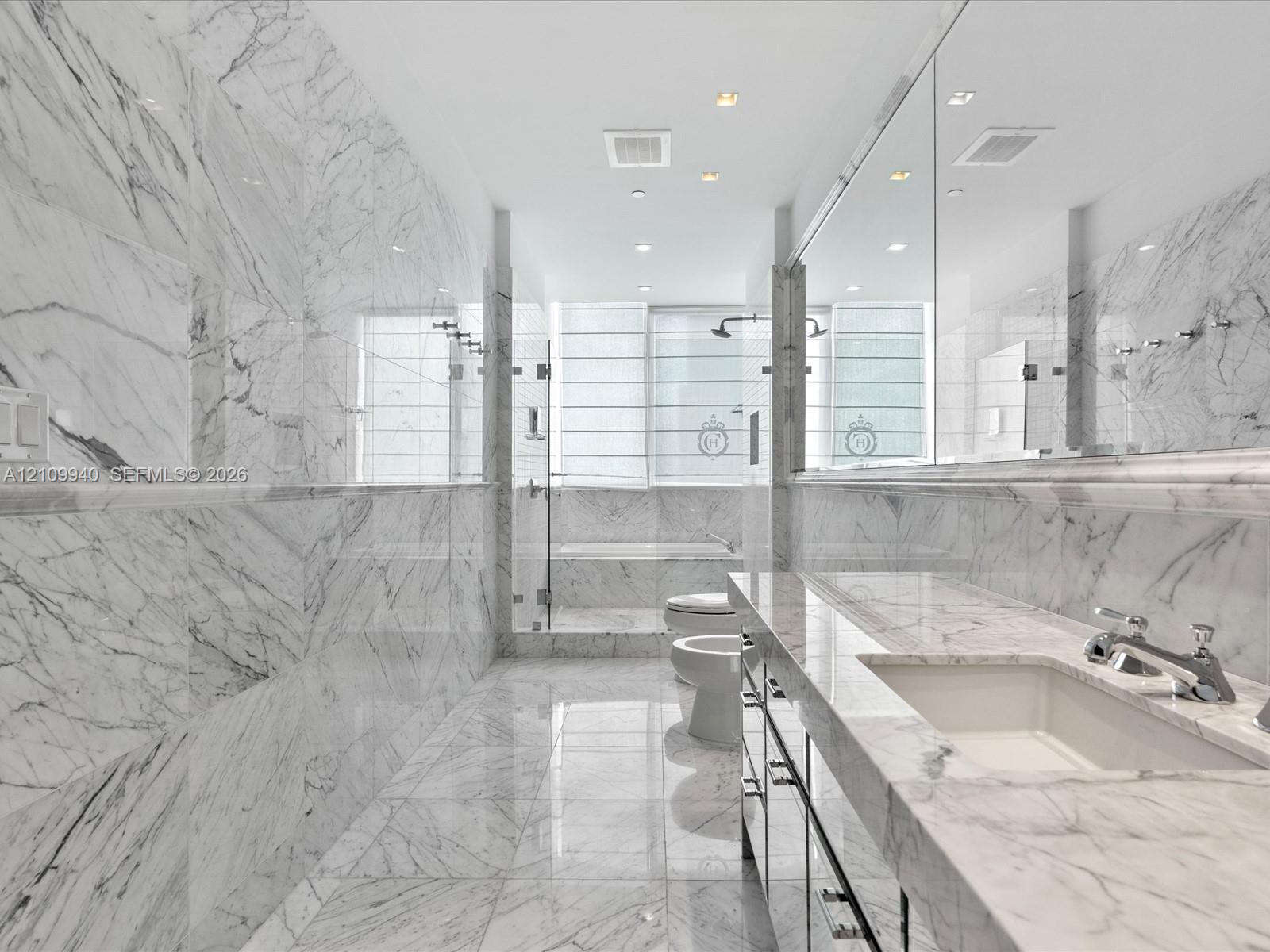Full-height stone wall tiling, expansive vanity with a stone countertop, integrated undermount sink, recessed ceiling lighting, and a glass-enclosed shower area