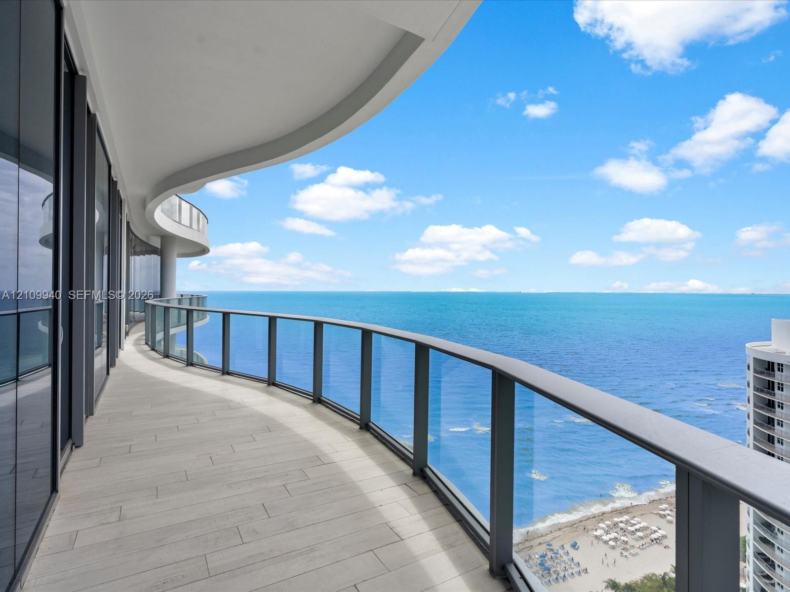 Curved balcony featuring tile flooring, full-height glass sliding doors, and a glass-paneled railing overlooking the ocean