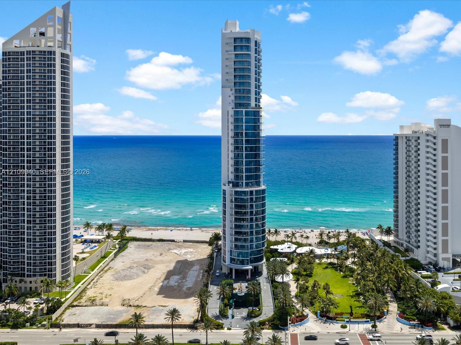 High-rise coastal tower featuring a glass-curtain facade, wraparound balconies, and direct proximity to the oceanfront